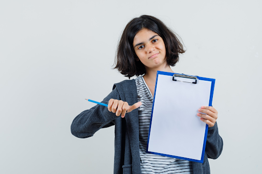 Pre‑teen holding a clipboard with a blank rubric and pencil, symbolizing clear criteria and measurable performance standards at TKA Ankuram.
